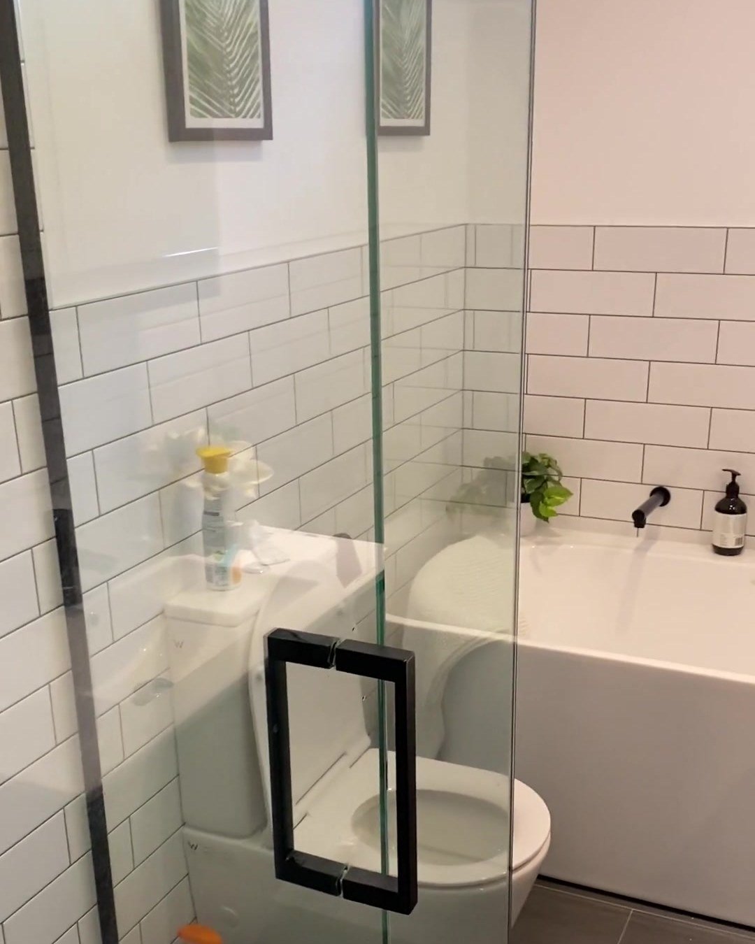 Half-height white subway tiles and a white bath seen through frameless shower glass, Albany