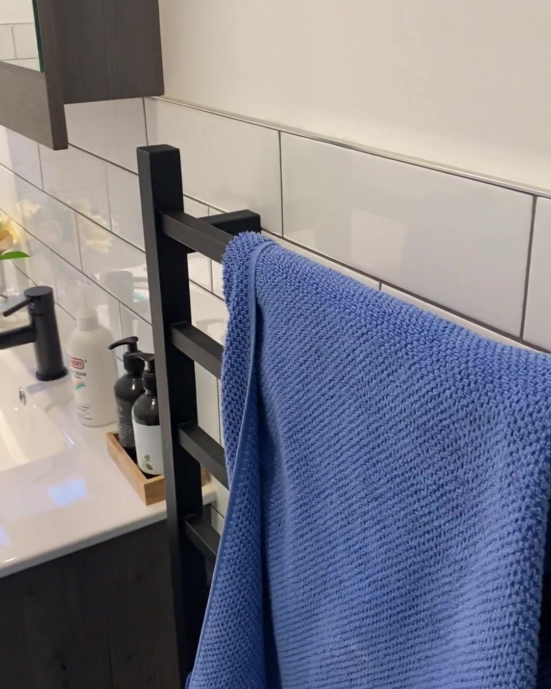 Black heated ladder towel rail on white subway tiles beside the vanity, Albany
