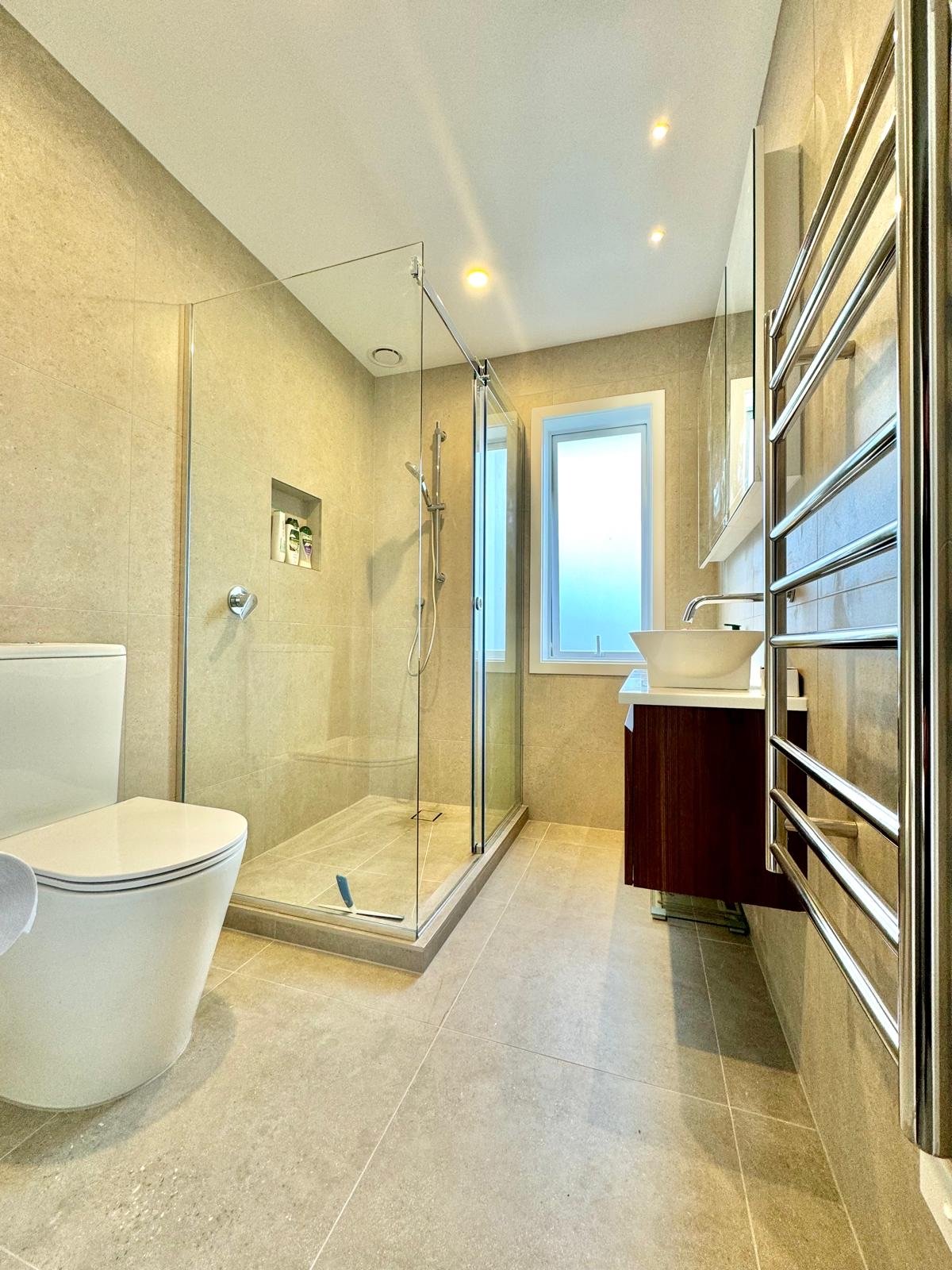 Finished bathroom with a corner glass shower, back-to-wall toilet and heated towel rail