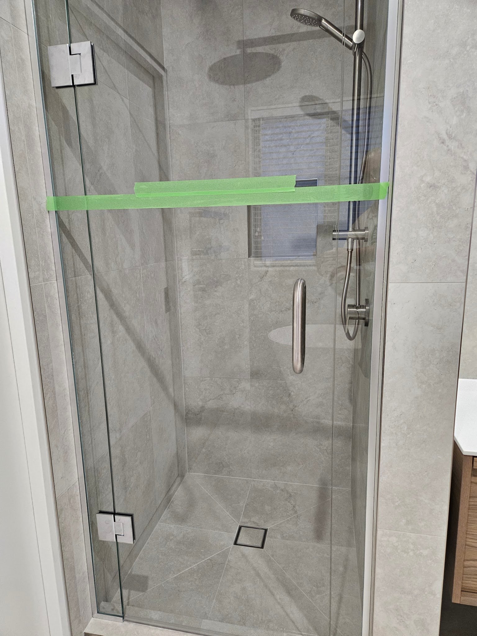 Frameless glass shower with a rain head and tiled niche, protective tape still on the glass