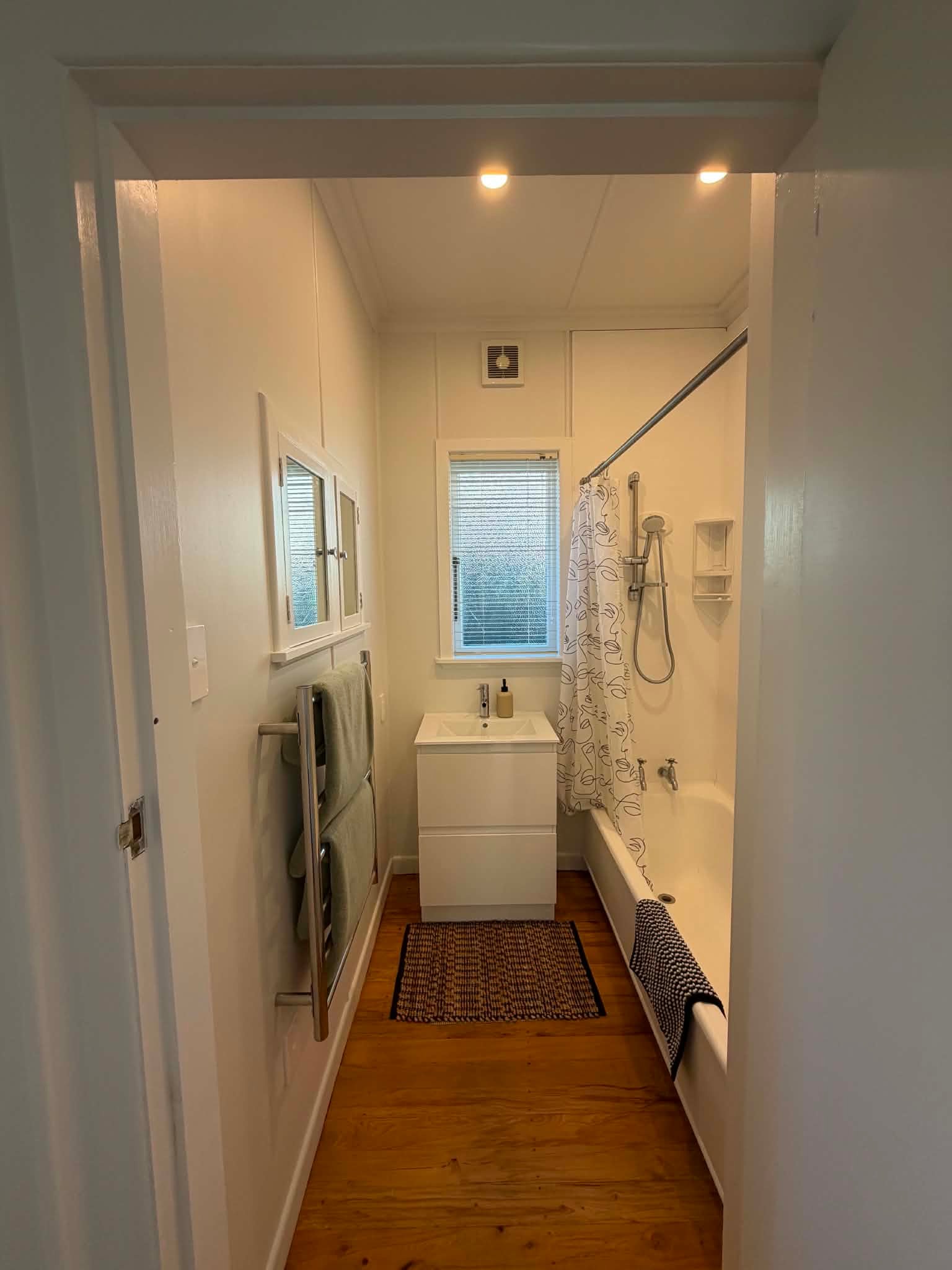 Narrow bathroom with a bath, white vanity and timber floor