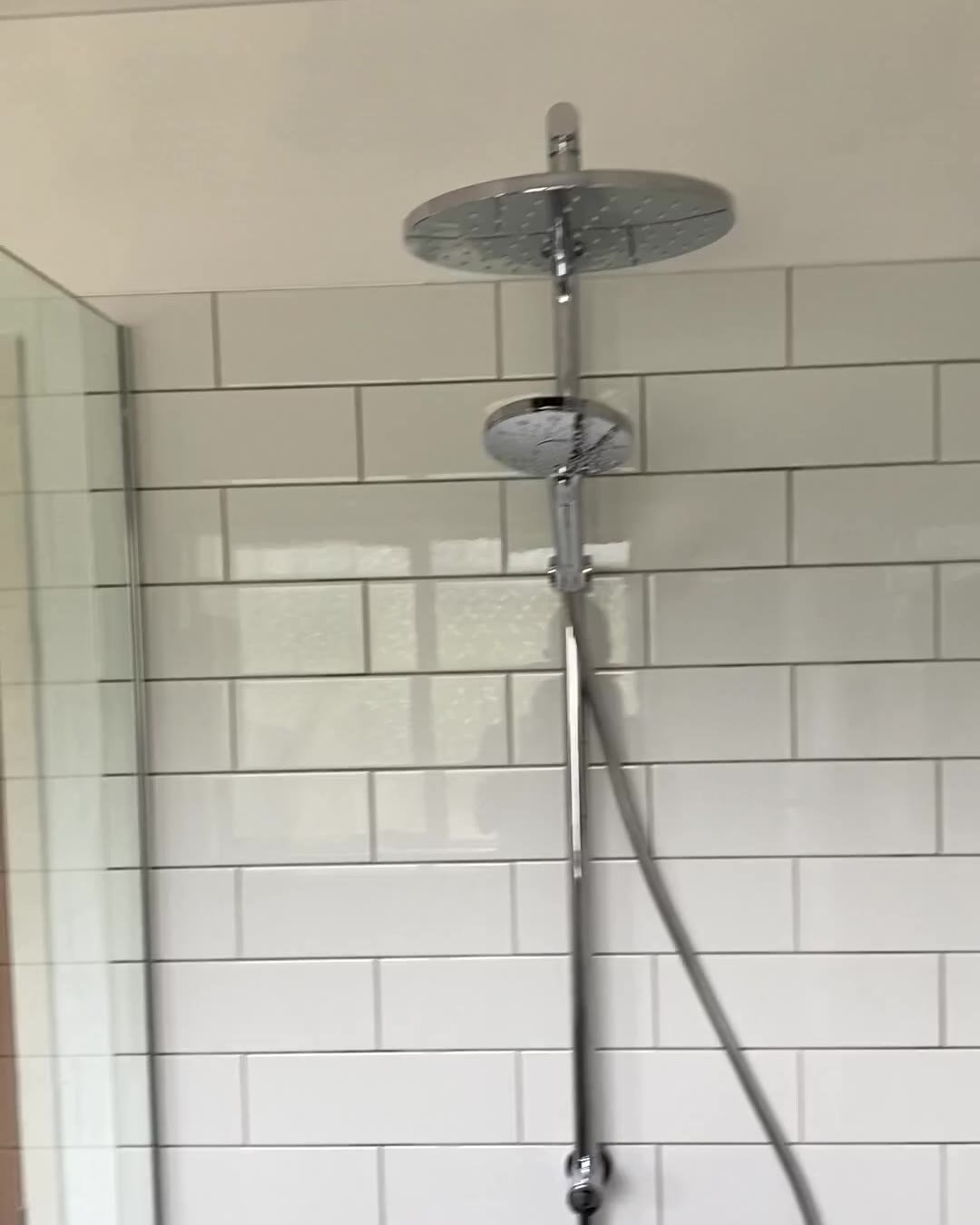 Chrome shower rail with overhead rain head and hand shower on white subway tiles