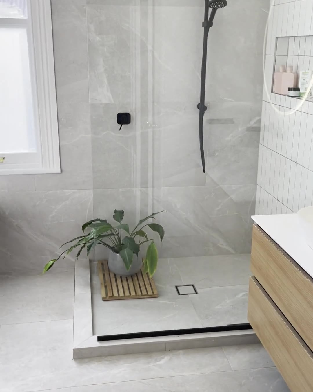 Walk-in shower with a black rail shower and a fixed glass panel beside a sash window, Mount Eden
