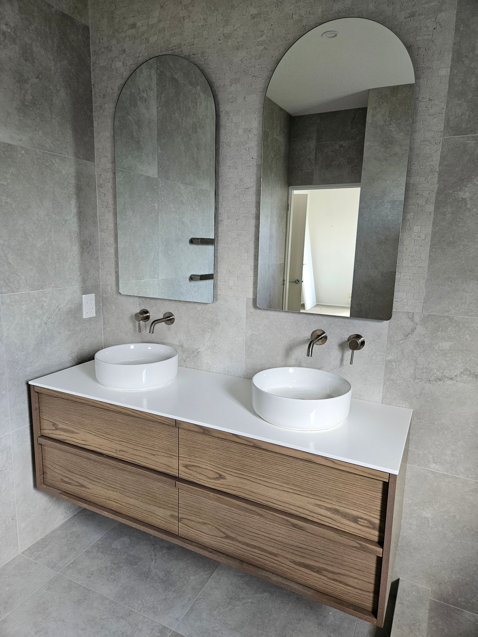 Floating timber double vanity with two round basins and arched mirrors in an Auckland bathroom renovated by Alchemy