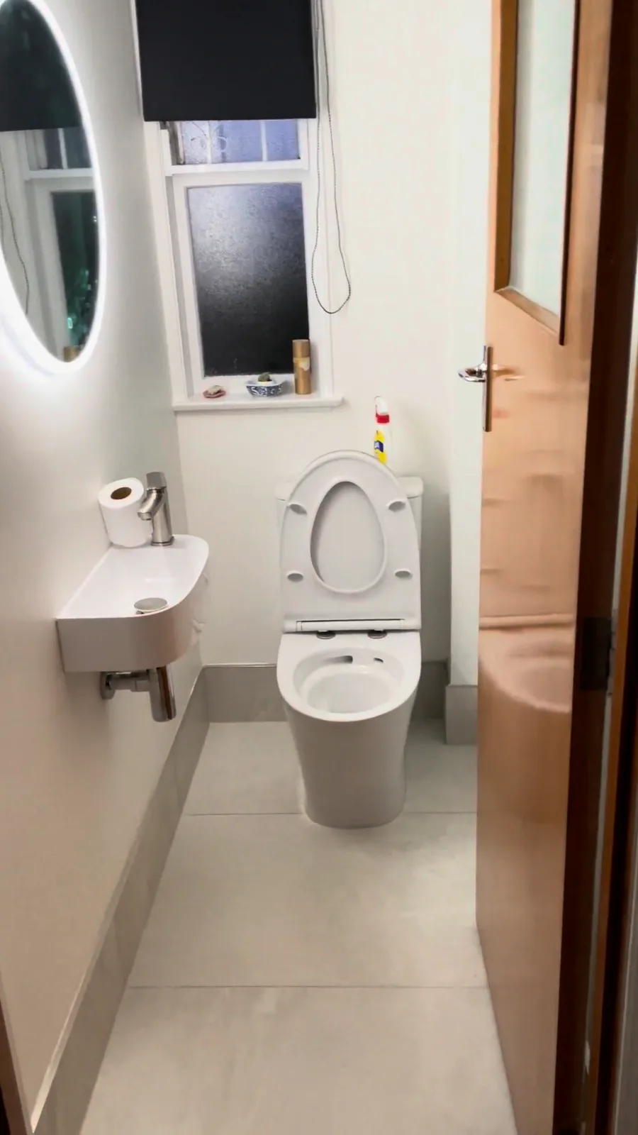 Separate toilet room with a wall-hung basin and round lit mirror in a Glendowie home