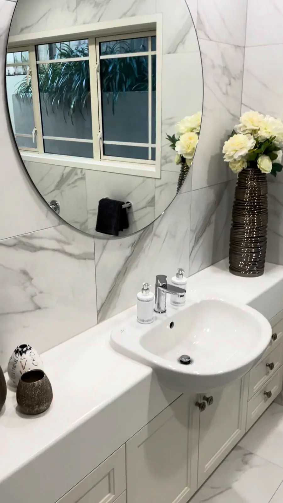 Round mirror above a white shaker vanity with marble-look wall tiles in a Kohimarama bathroom