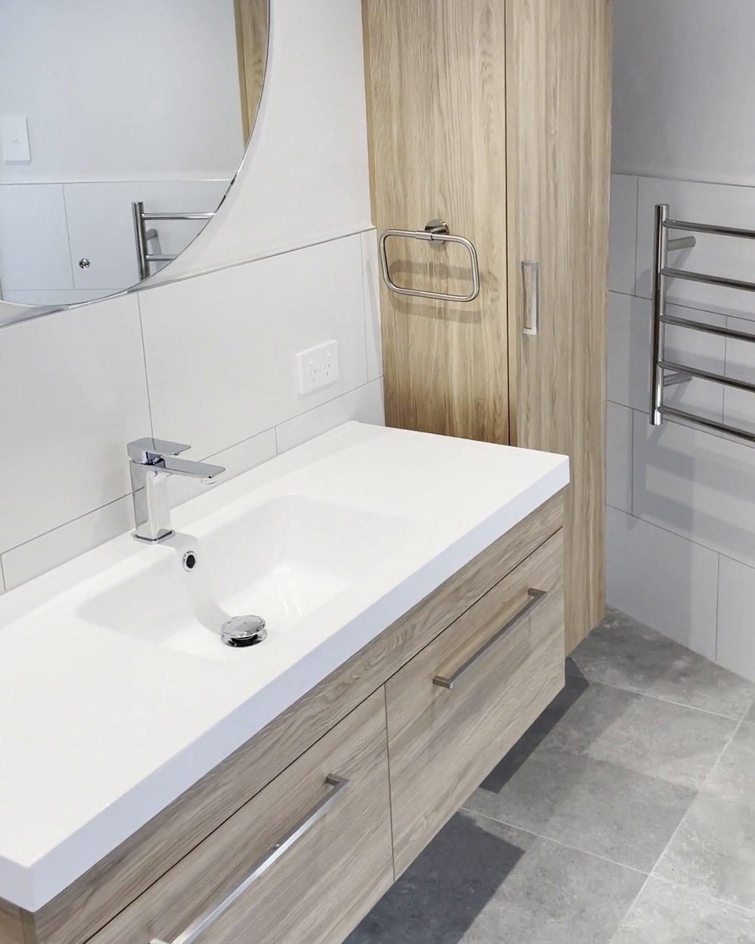 Wall-hung oak-look vanity with a round mirror and a tall oak-look cabinet in a renovated Parnell bathroom