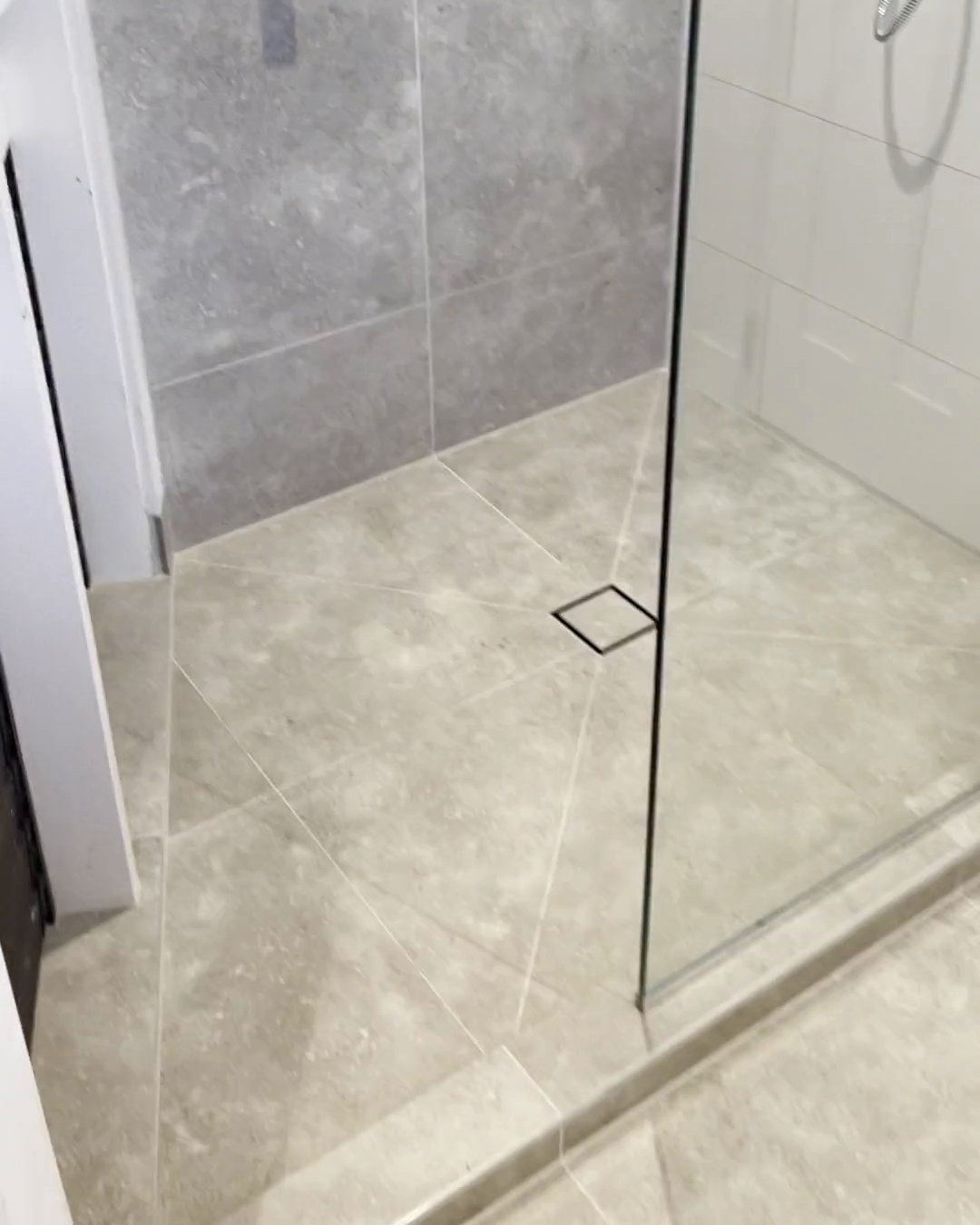 Square tile-insert shower drain and frameless glass panel on pale grey floor tiles, Parnell