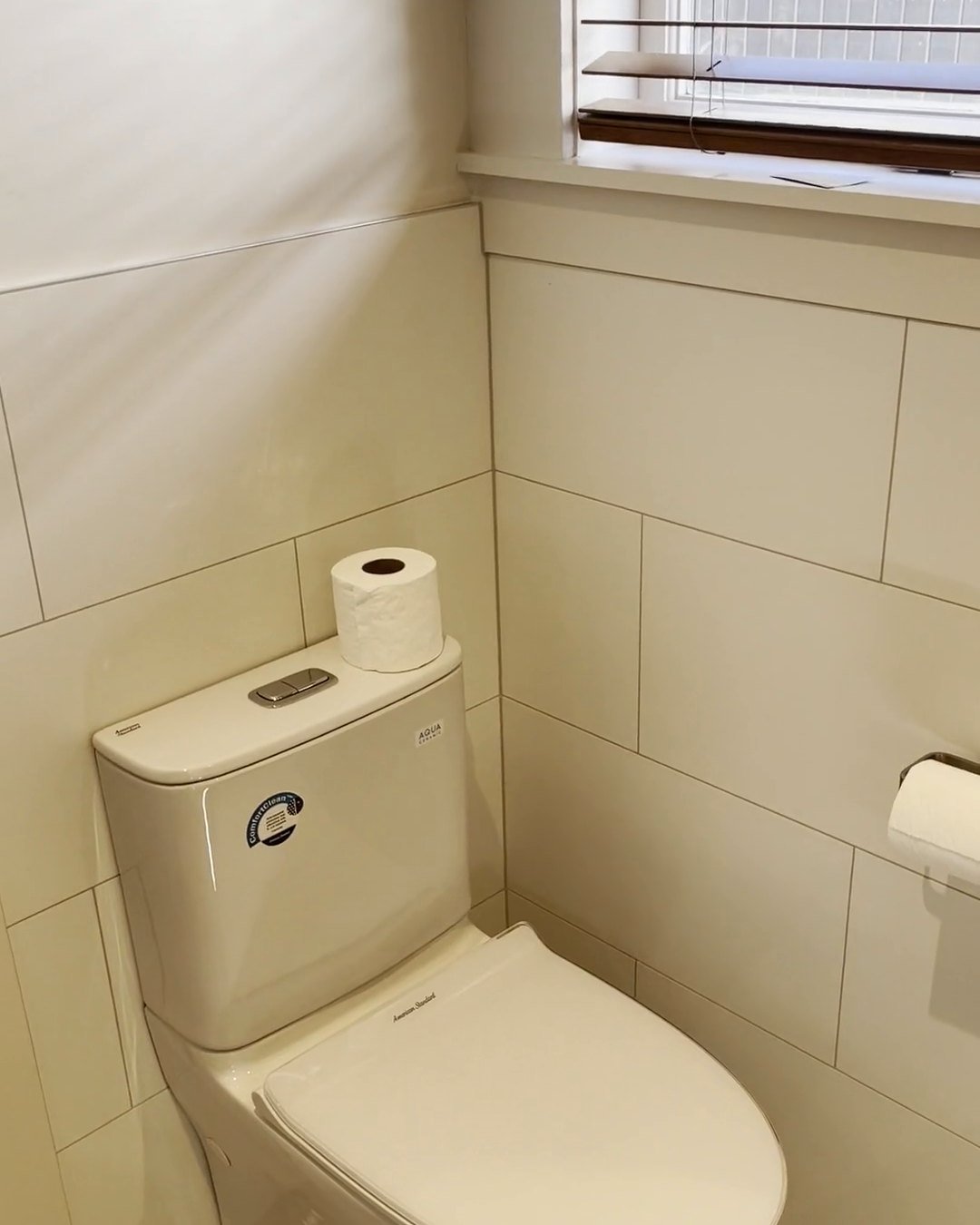 Close-coupled toilet under a timber window with white brick-pattern wall tiles, Parnell bathroom