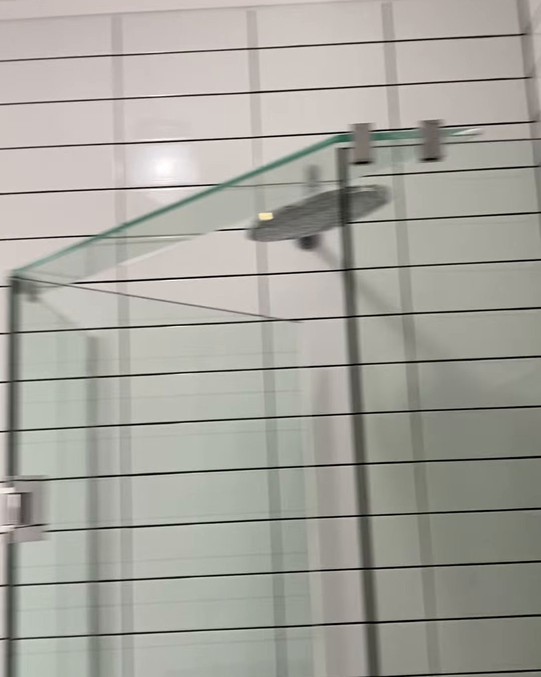 Frameless corner shower with an angled glass front and a rain shower head in a white tiled Ranui bathroom