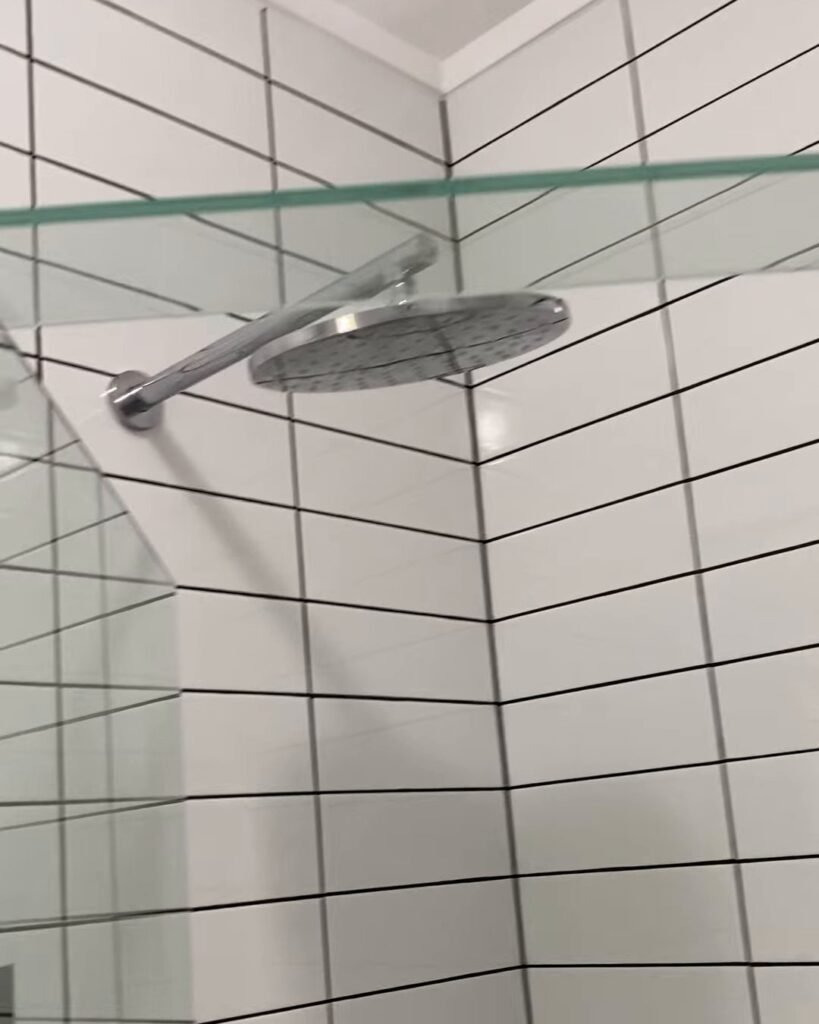 Ranui bathroom renovation rain shower head Round chrome rain shower head on a wall arm above white tiles with charcoal grout, Ranui