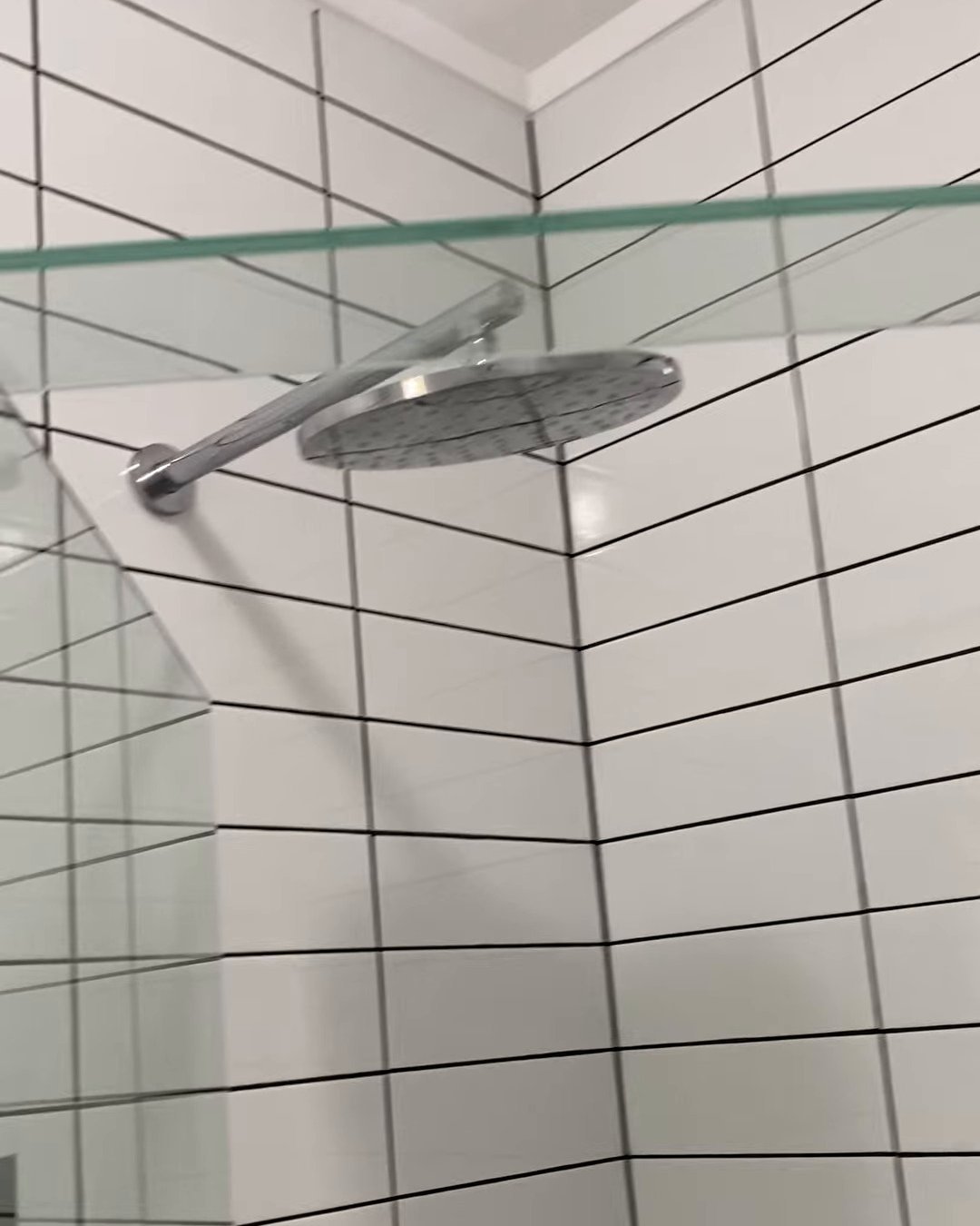 Round chrome rain shower head on a wall arm above white tiles with charcoal grout, Ranui