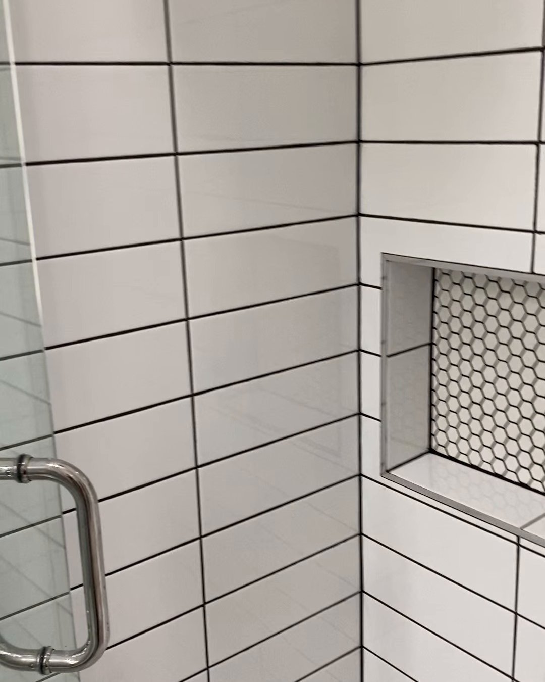 Shower niche lined with white hexagon mosaic beside a chrome glass door handle, Ranui bathroom