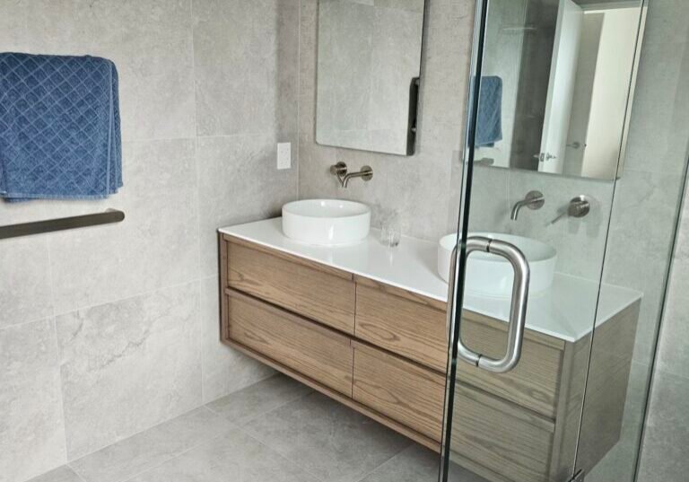 Timber double vanity with round basins and arched mirrors beside a glass shower