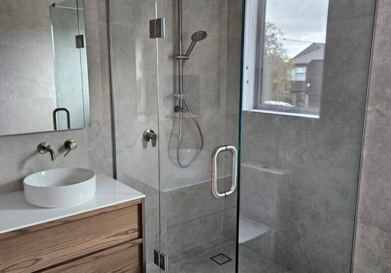 Corner glass shower with brushed nickel rail shower and grey tiles Corner glass shower with brushed nickel rail shower and grey tiles