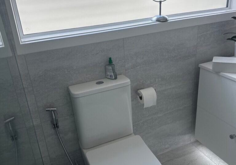 Back-to-wall toilet in a grey-tiled bathroom under a frosted window Back-to-wall toilet in a grey-tiled bathroom under a frosted window