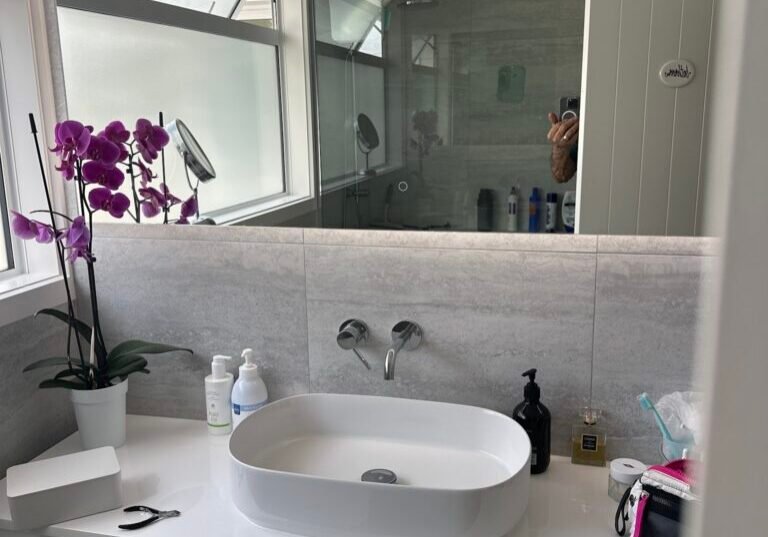 White vanity with an oval vessel basin and wall-mounted tap under a wide mirror White vanity with an oval vessel basin and wall-mounted tap under a wide mirror