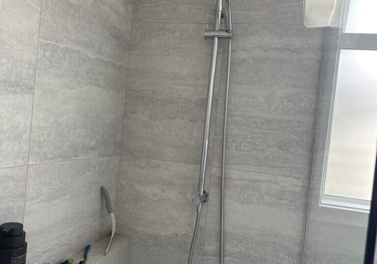 Tiled shower with a chrome rail shower and grey stone-look tiles Tiled shower with a chrome rail shower and grey stone-look tiles