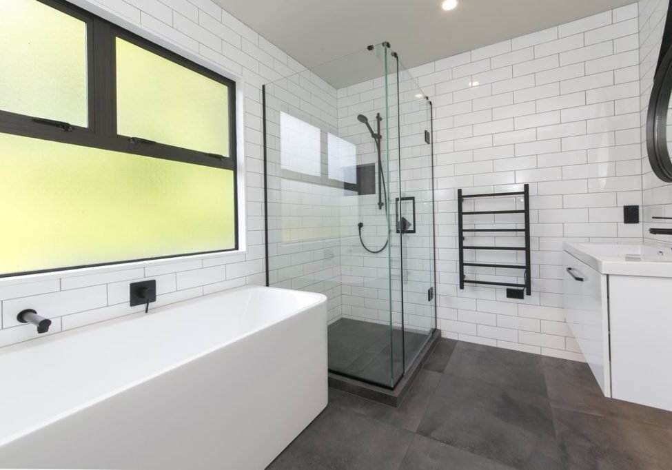 Black and white bathroom with a bath under frosted windows and glass shower in Epsom