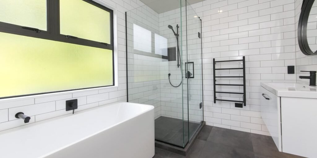 Black and white bathroom with a bath under frosted windows and glass shower in Epsom