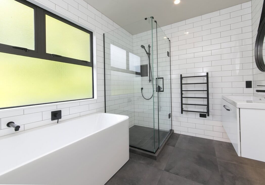 bathroom renovations auckland nz Black and white bathroom with a bath under frosted windows and glass shower in Epsom