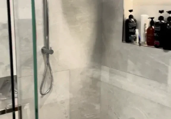 Walk-in shower with a rail shower, rain head and lit niche in large marble-look tiles, Glendowie