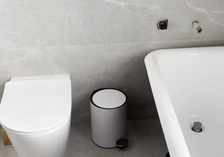 mount-eden-bathroom-toilet Back-to-wall toilet with a black flush plate on grey stone-look tiles, Mount Eden