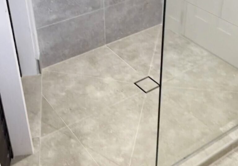 Parnell bathroom shower drain and glass Square tile-insert shower drain and frameless glass panel on pale grey floor tiles, Parnell