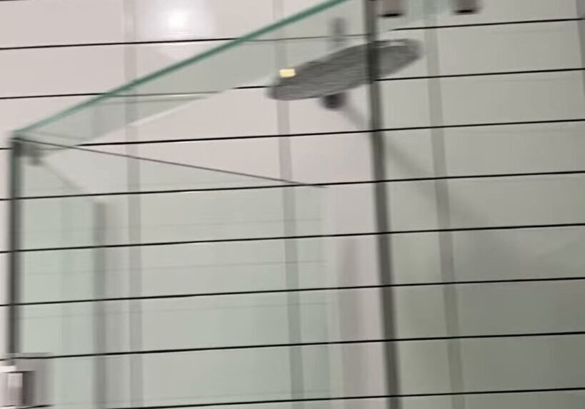 Frameless corner shower with an angled glass front and a rain shower head in a white tiled Ranui bathroom